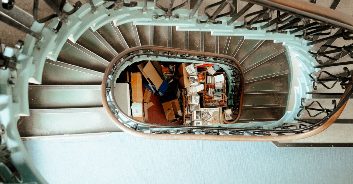 Blick von oben auf eine Wendeltreppe, in deren Mitte Kisten und verstreute Gegenstände liegen.