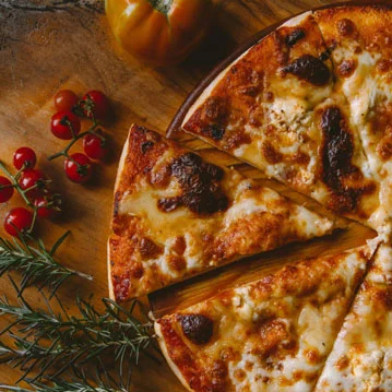 Auf einem Holzbrett liegt eine halbe Pizza magaritta mit Käse und nebenan liegt kleine Tomaten und Rosmarin